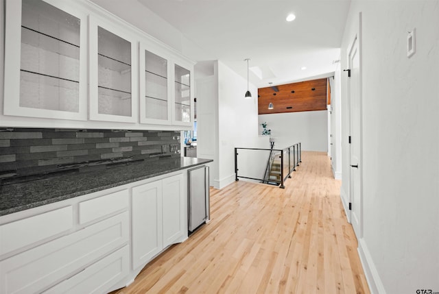 kitchen with tasteful backsplash, white cabinets, dark stone counters, glass insert cabinets, and hanging light fixtures