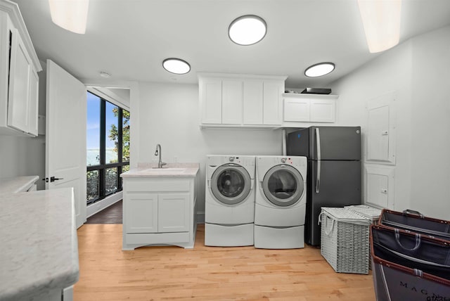 laundry area with separate washer and dryer, light wood-style floors, cabinet space, and a sink