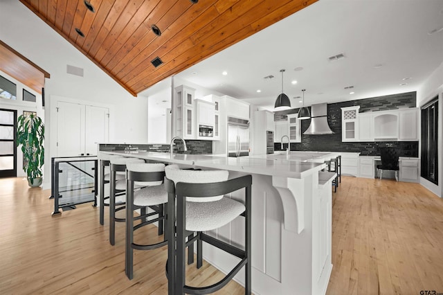 kitchen with built in appliances, wall chimney exhaust hood, glass insert cabinets, and white cabinetry