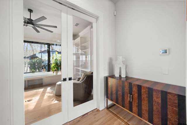 interior space with a ceiling fan, french doors, visible vents, and wood finished floors