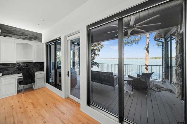 interior space featuring light wood finished floors, built in study area, ceiling fan, a water view, and recessed lighting