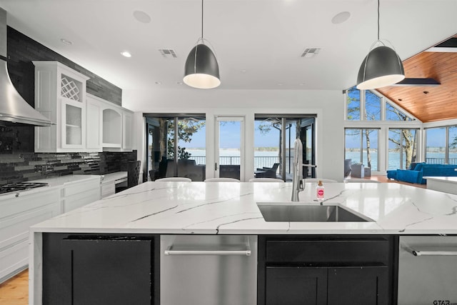 kitchen featuring wall chimney exhaust hood, an island with sink, and white cabinetry