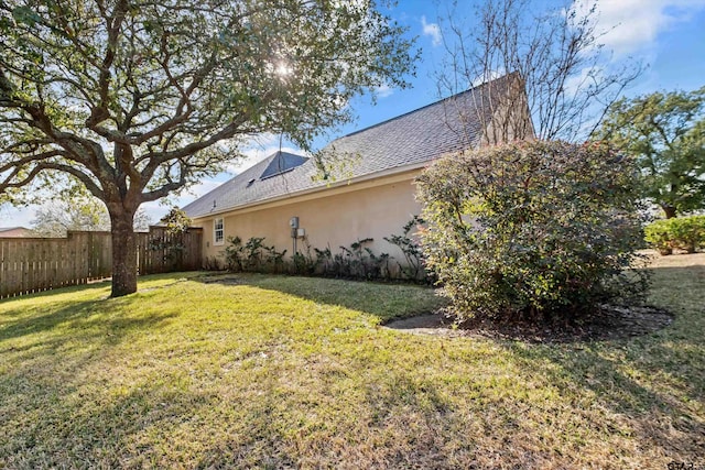 view of side of home with fence, a lawn, and stucco siding