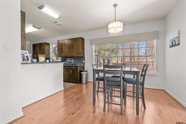 dining space featuring light wood-style flooring, a notable chandelier, baseboards, and visible vents