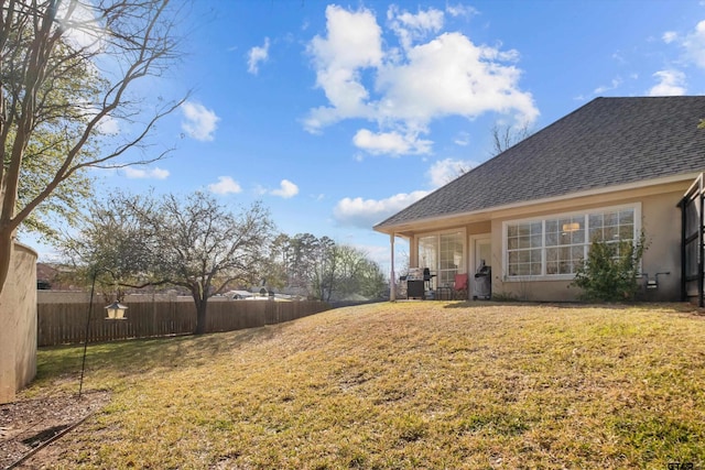 exterior space with stucco siding, a lawn, a shingled roof, and fence