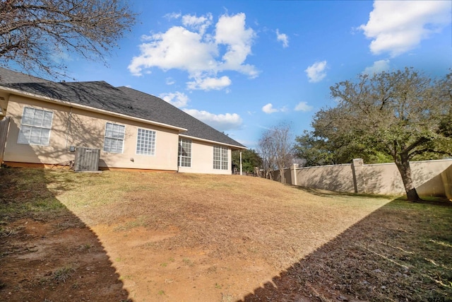 rear view of property featuring stucco siding, central air condition unit, a yard, and fence