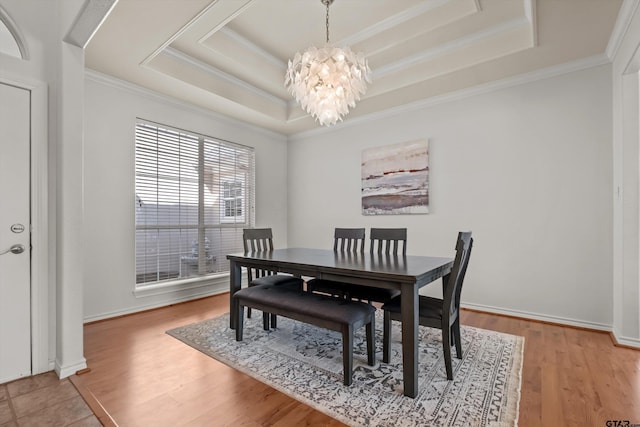 dining space featuring a chandelier, light wood-type flooring, and a raised ceiling