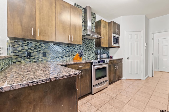 kitchen with dark stone countertops, light tile patterned floors, appliances with stainless steel finishes, wall chimney range hood, and backsplash