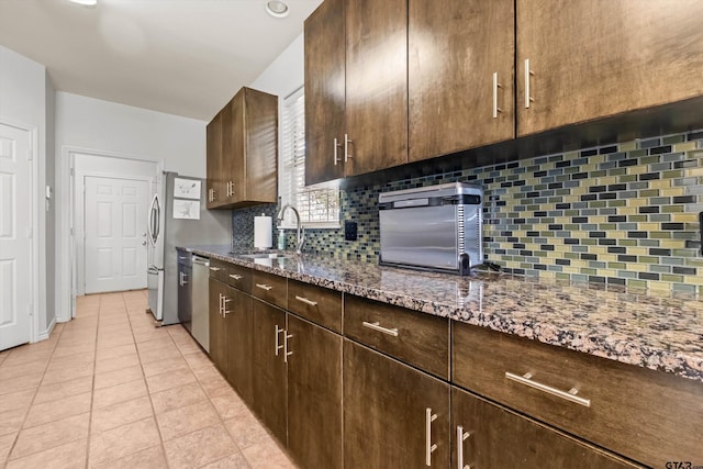 kitchen featuring backsplash, light tile patterned flooring, stone countertops, stainless steel appliances, and a sink