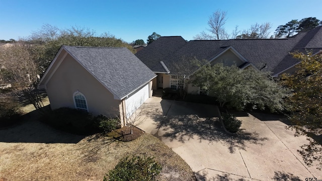 view of property exterior with concrete driveway, an attached garage, roof with shingles, and stucco siding