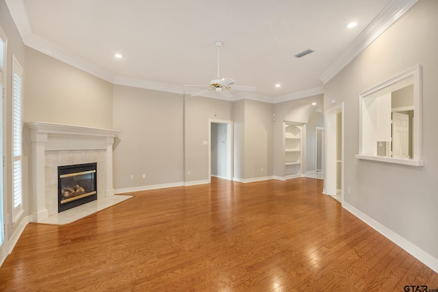 unfurnished living room with a tiled fireplace, crown molding, a healthy amount of sunlight, and light hardwood / wood-style flooring