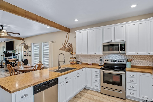 kitchen featuring stainless steel appliances, butcher block counters, beam ceiling, sink, and white cabinets