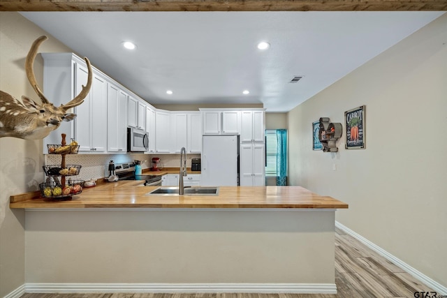 kitchen with tasteful backsplash, stainless steel appliances, white cabinetry, sink, and kitchen peninsula