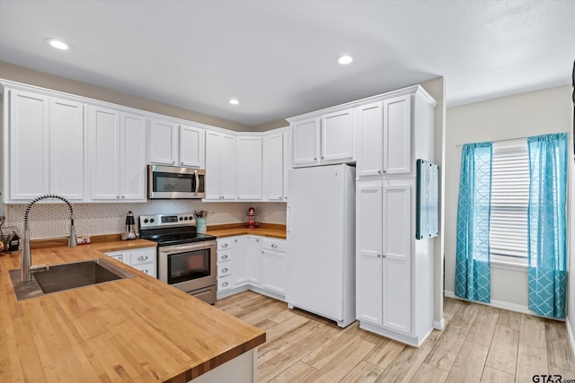 kitchen with butcher block countertops, white cabinetry, appliances with stainless steel finishes, and sink