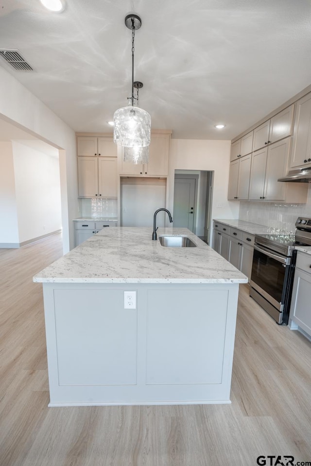 kitchen featuring stainless steel electric range, sink, an island with sink, backsplash, and pendant lighting