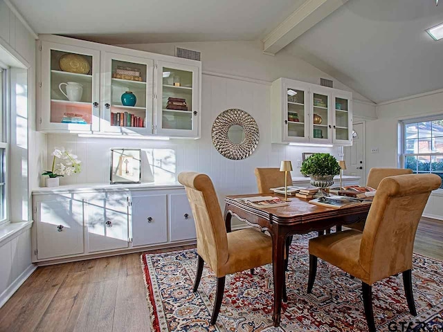 dining room featuring light wood-type flooring and vaulted ceiling with beams