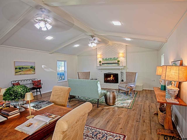 living room featuring vaulted ceiling with beams, ceiling fan, wood-type flooring, and a brick fireplace