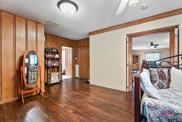 interior space with a textured ceiling, dark hardwood / wood-style flooring, wooden walls, ceiling fan, and brick wall