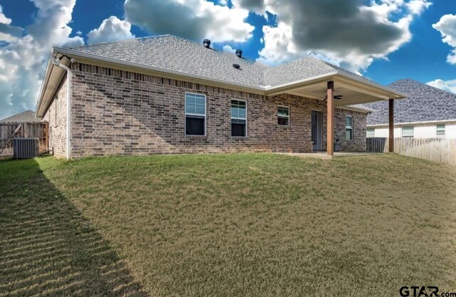 rear view of house with central air condition unit and a lawn