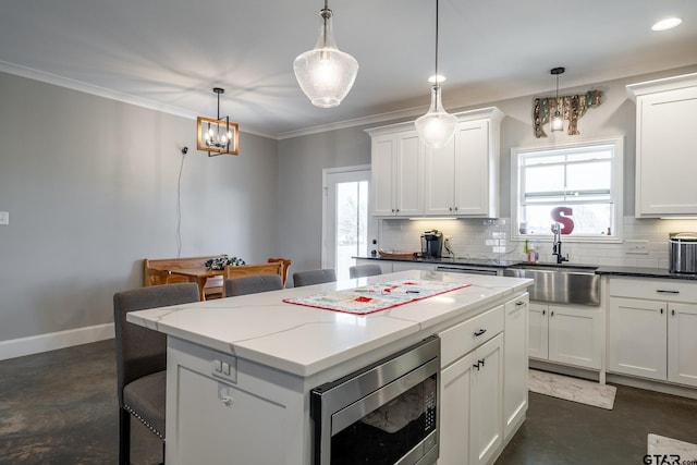 kitchen with white cabinetry, pendant lighting, stainless steel microwave, and sink