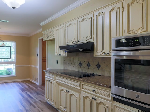 8310 Columbia Dr, Tyler, TX 75703 - kitchen featuring cream cabinets, stainless steel oven, under cabinet range hood, decorative backsplash, and black electric cooktop
