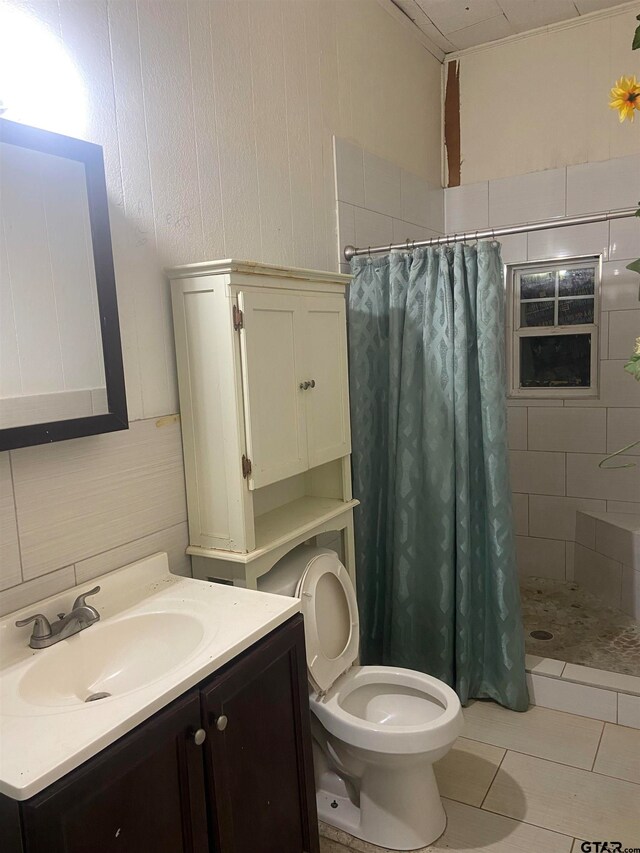 bathroom featuring curtained shower, tile patterned floors, toilet, vanity, and tile walls