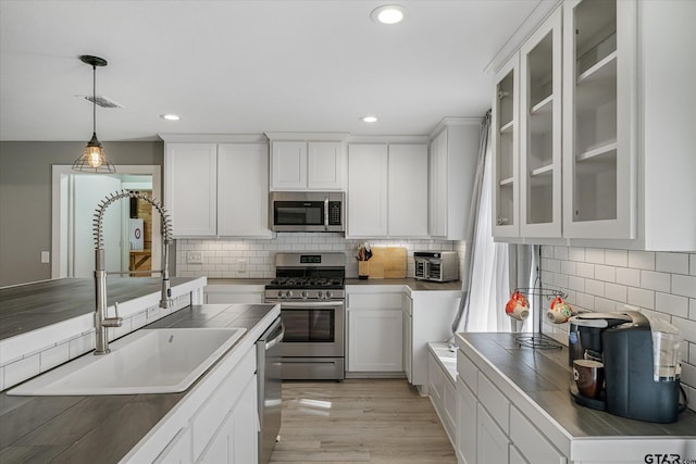 kitchen with sink, white cabinets, appliances with stainless steel finishes, and pendant lighting