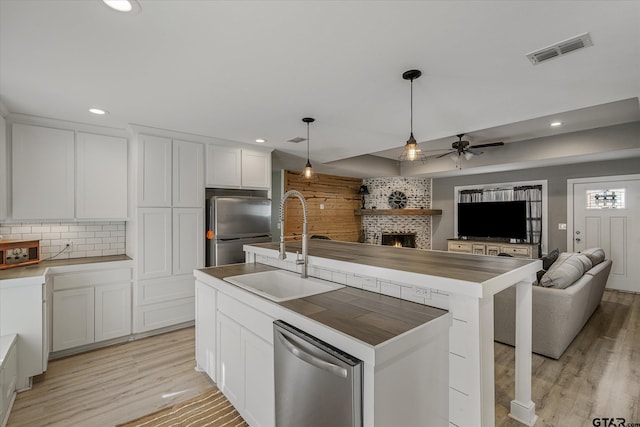 kitchen with hanging light fixtures, white cabinets, sink, stainless steel appliances, and a center island with sink