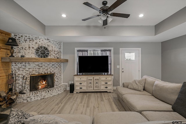 living room featuring a large fireplace, light wood-type flooring, ceiling fan, and a tray ceiling