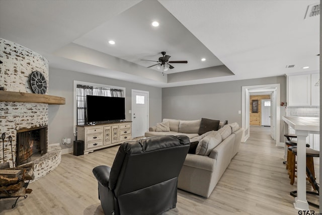 living room featuring a large fireplace, light wood-type flooring, ceiling fan, and a raised ceiling