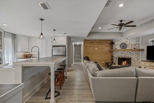 living room featuring sink, ceiling fan, a brick fireplace, and light hardwood / wood-style flooring