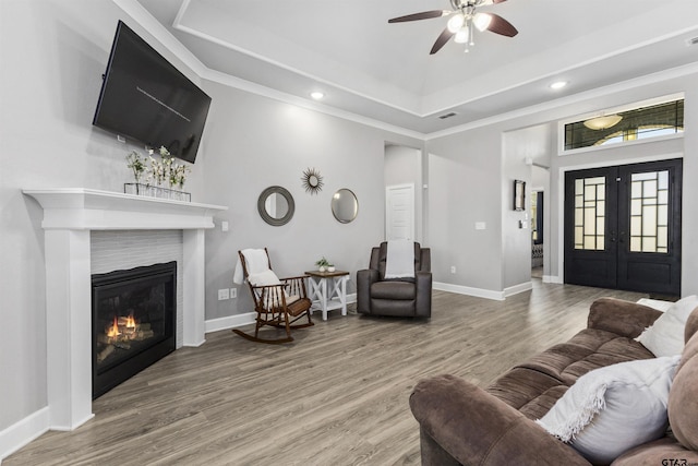 living room with crown molding, a fireplace, hardwood / wood-style flooring, french doors, and a raised ceiling