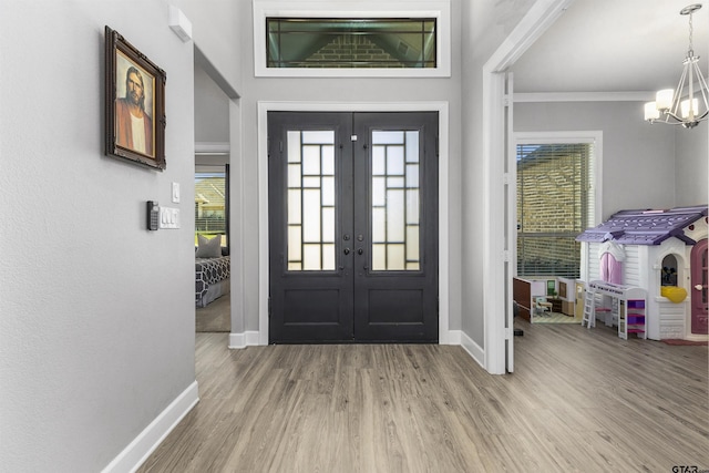 foyer entrance with ornamental molding, hardwood / wood-style floors, an inviting chandelier, and french doors