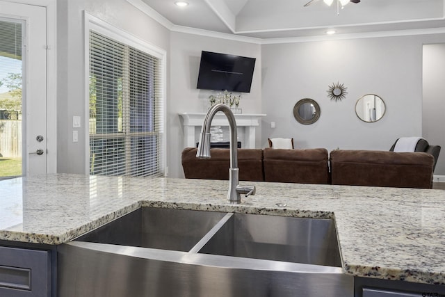 kitchen featuring sink, ceiling fan, light stone counters, and crown molding