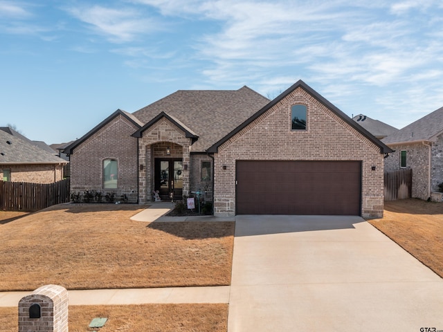 french country inspired facade featuring brick siding, fence, concrete driveway, french doors, and a garage