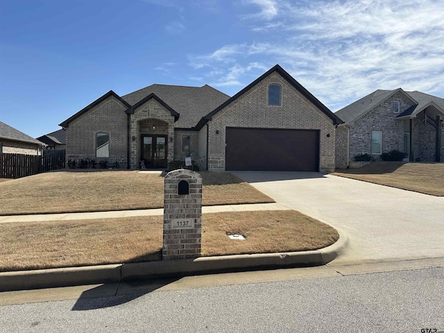 french country inspired facade with fence, driveway, french doors, a garage, and brick siding