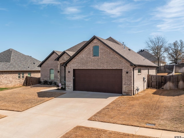 french country home with a garage, brick siding, concrete driveway, and fence