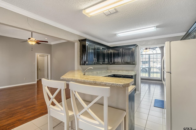 kitchen with light tile patterned floors, visible vents, dark cabinets, freestanding refrigerator, and a peninsula