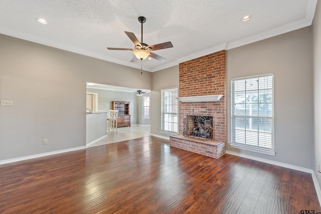 unfurnished living room with a wealth of natural light, crown molding, a brick fireplace, and wood finished floors