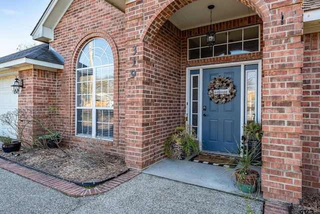 view of exterior entry featuring an attached garage and brick siding