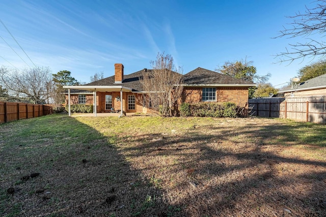 back of property with a fenced backyard, brick siding, a yard, a chimney, and a patio area