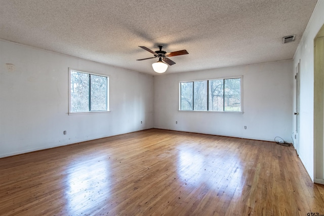 spare room with ceiling fan, a wealth of natural light, wood-type flooring, and visible vents