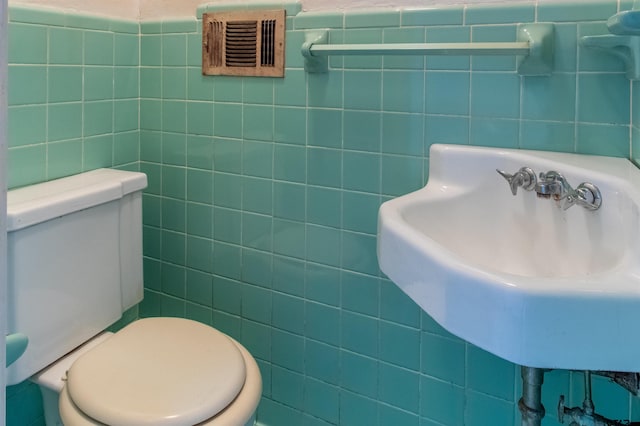 half bath featuring toilet, a sink, visible vents, and tile walls