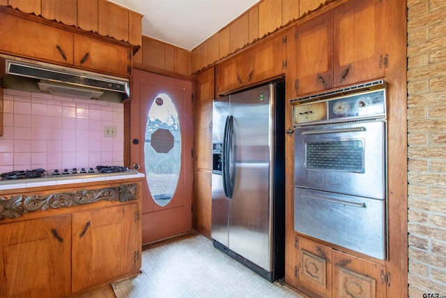 kitchen featuring brown cabinets, tile countertops, light floors, stainless steel appliances, and under cabinet range hood