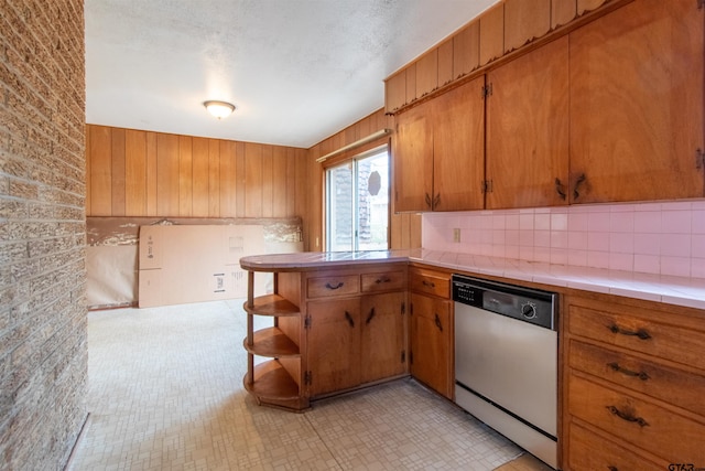 kitchen featuring dishwasher, tile countertops, brown cabinets, wood walls, and open shelves