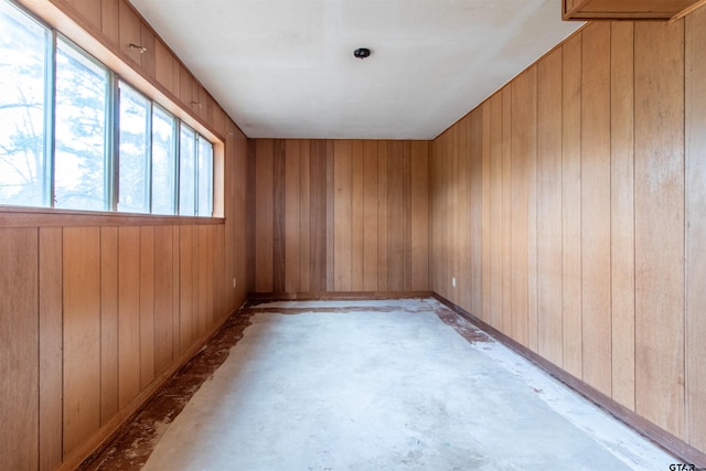 empty room with wood walls and unfinished concrete flooring