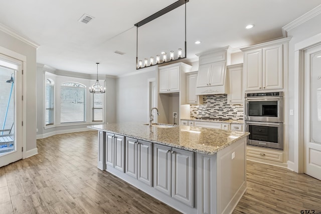 kitchen with a kitchen island with sink, sink, white cabinetry, and light stone countertops