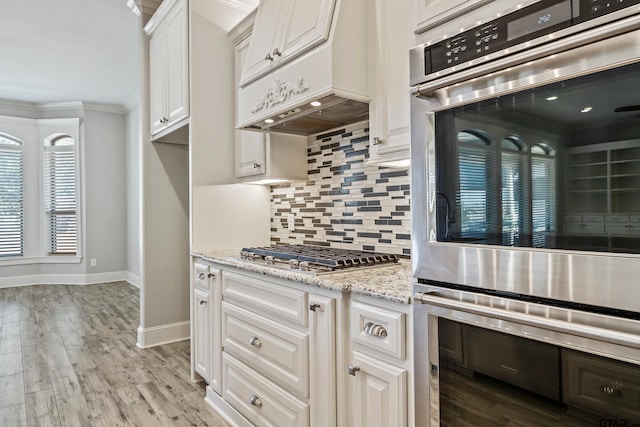 kitchen featuring light hardwood / wood-style flooring, appliances with stainless steel finishes, light stone counters, tasteful backsplash, and white cabinets