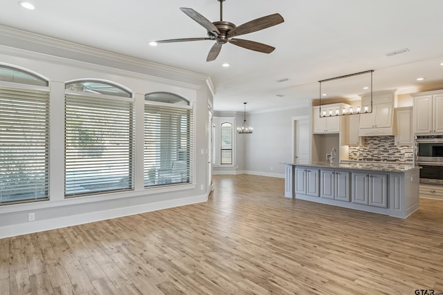 kitchen with crown molding, decorative light fixtures, a kitchen island with sink, double oven, and ceiling fan with notable chandelier