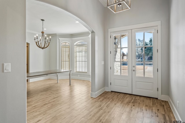 foyer featuring ornamental molding, a notable chandelier, light hardwood / wood-style floors, and french doors